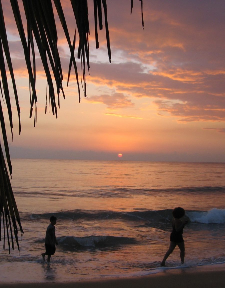 A woman and child walking in shallow waves on a beach at sunset