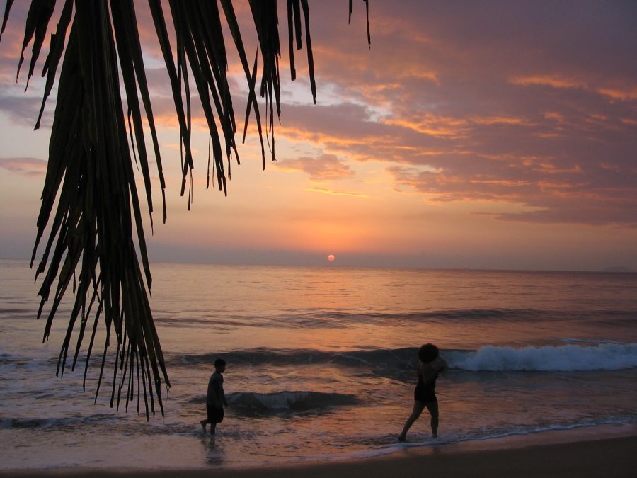 A woman and child walking in shallow waves on a beach at sunset