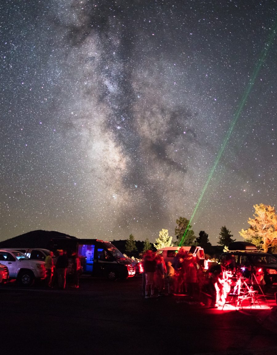 A park ranger points a green laser at the Milky Way for a crowd at a guided star party