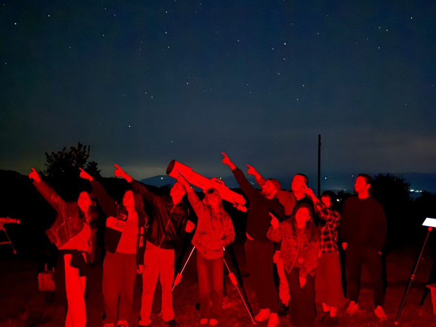 A group silhouetted in red light looking up at a star-filled night sky