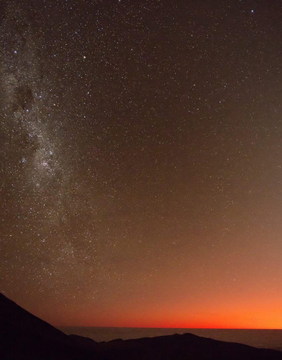 A dramatic fiery twilight sky with the Milky Way already visible over an observatory ridge