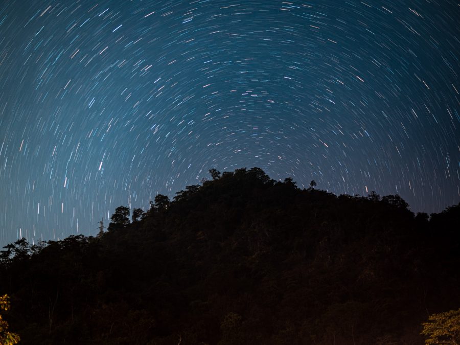 Circular star trails over a silhouetted forested ridge, long exposure