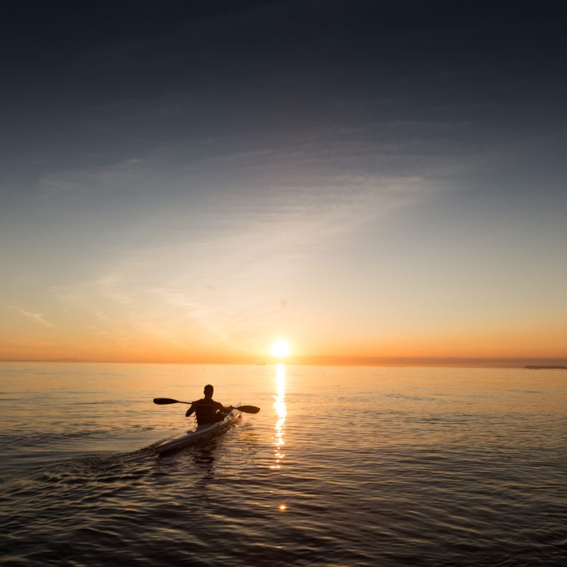 A kayaker silhouetted on calm water at sunset, seen from behind