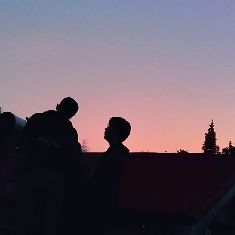 Silhouettes of a group setting up a portable telescope at dusk
